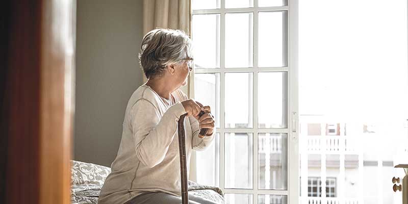 Thoughtful Senior Woman Leaning On Walking Stick While Sitting O